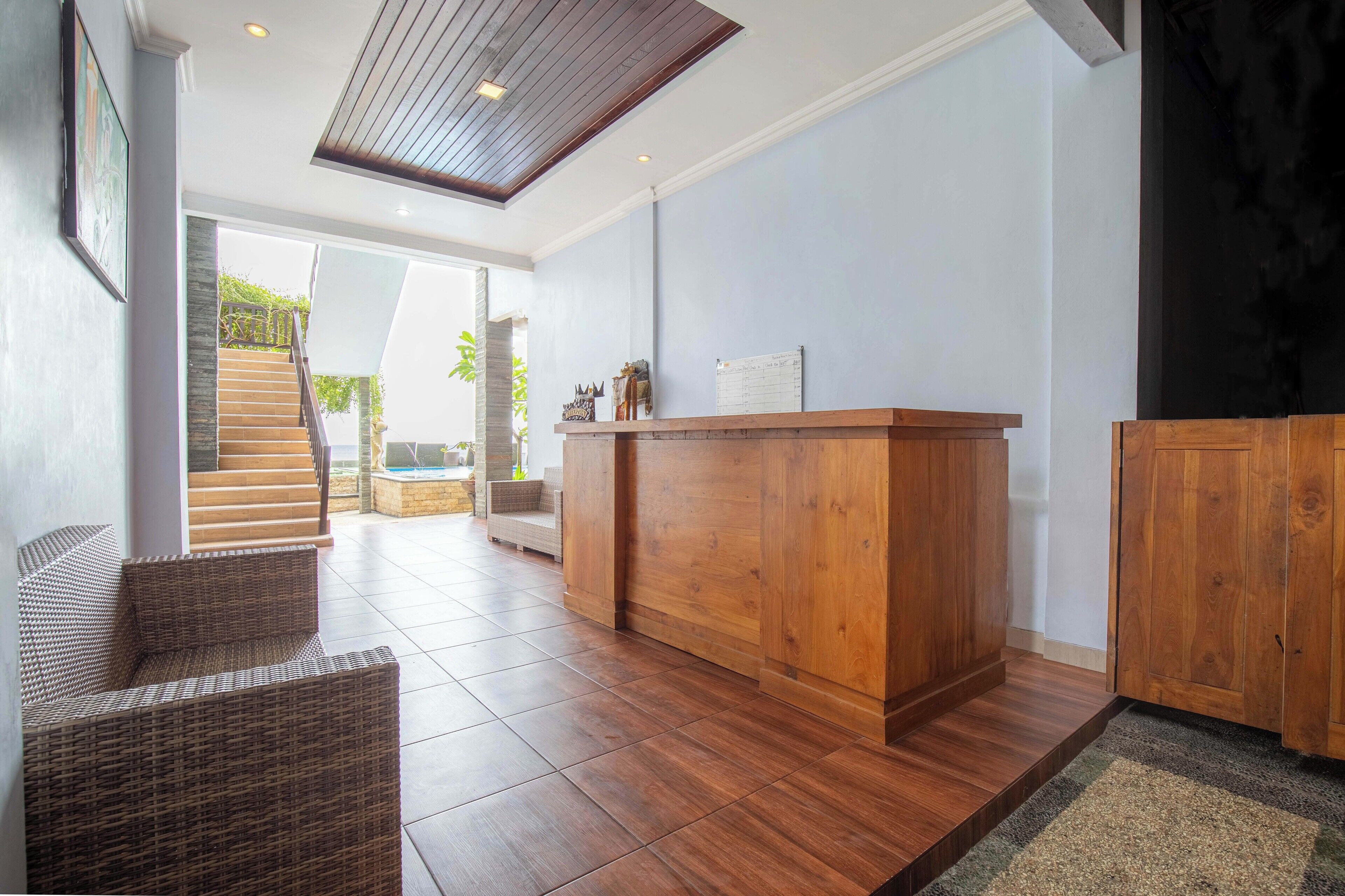 Un área de recepción con un mostrador de madera, mobiliario de mimbre y una escalera que lleva a un espacio al aire libre.