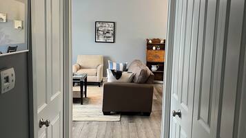 A hallway leading to a living room with a sofa, a ceiling fan, and a framed picture on the wall.