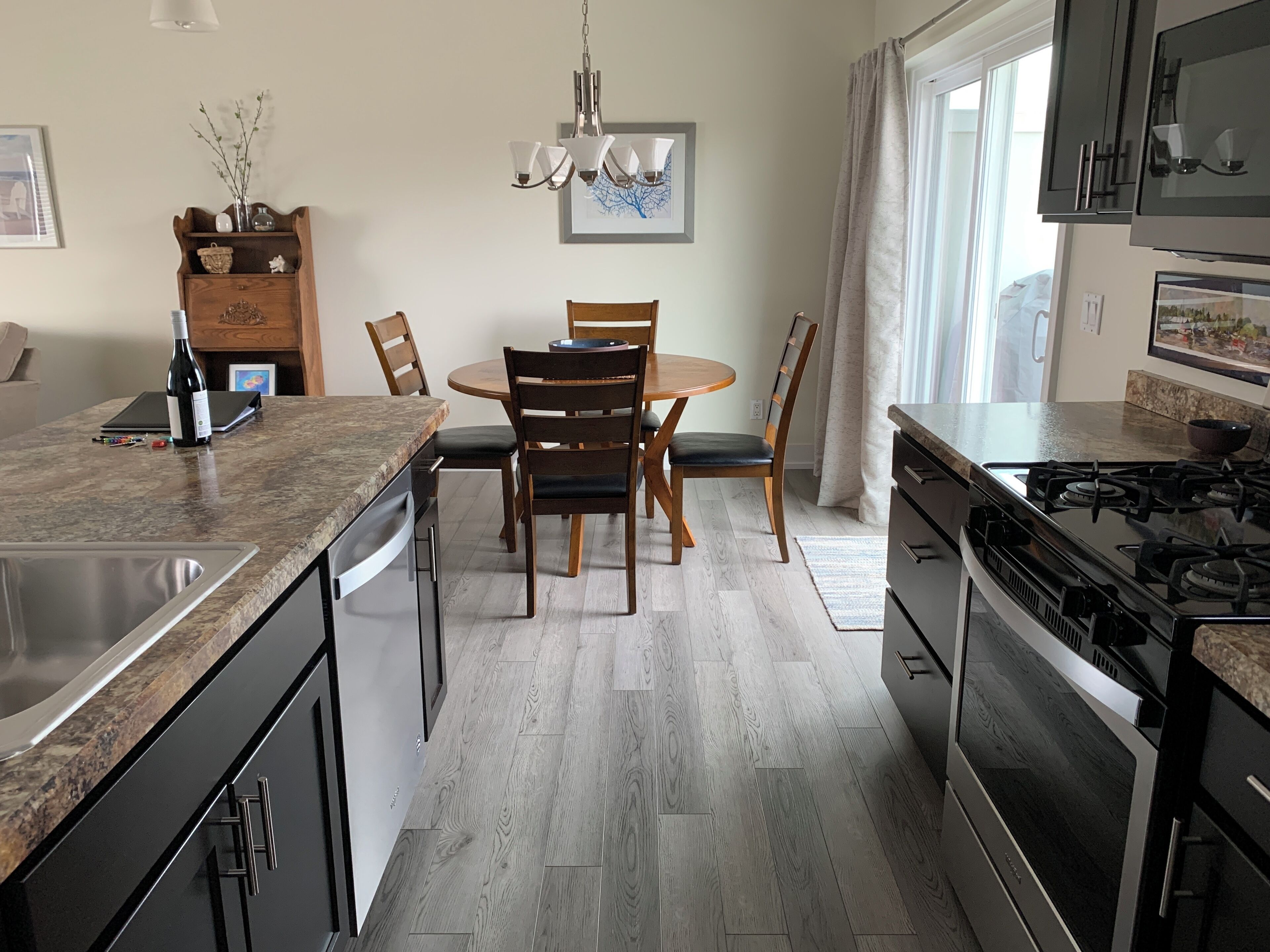 A modern kitchen with a granite countertop, stainless steel appliances, and a dining area with wooden chairs and a round table.