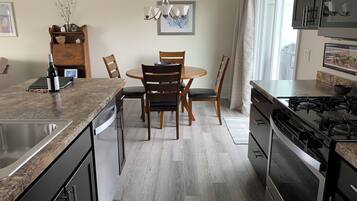 A modern kitchen with a granite countertop, stainless steel appliances, and a dining area with wooden chairs and a round table.