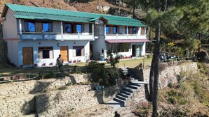 A two-story building with a green roof, stone steps leading up to the entrance, and a balcony with railings. - Binsar View Homestay (Almora)