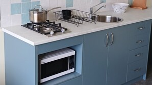 Una cocina compacta con estufa a gas, microondas, pileta y escurreplatos.