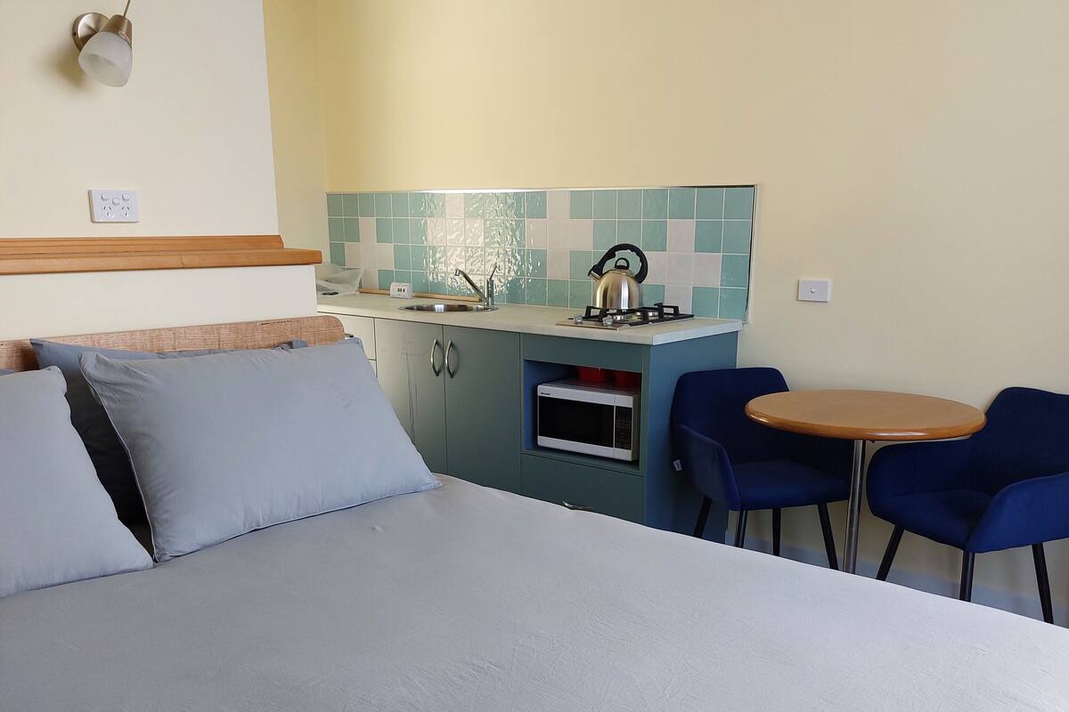 Un dormitorio con cama, una kitchenette pequeña con estufa y microondas, y un comedor con mesa y sillas.