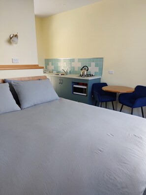 A bedroom with a bed, a small kitchenette with a stove and microwave, and a dining area with a table and chairs. - Near and Far Nature Stay (Neerim East)