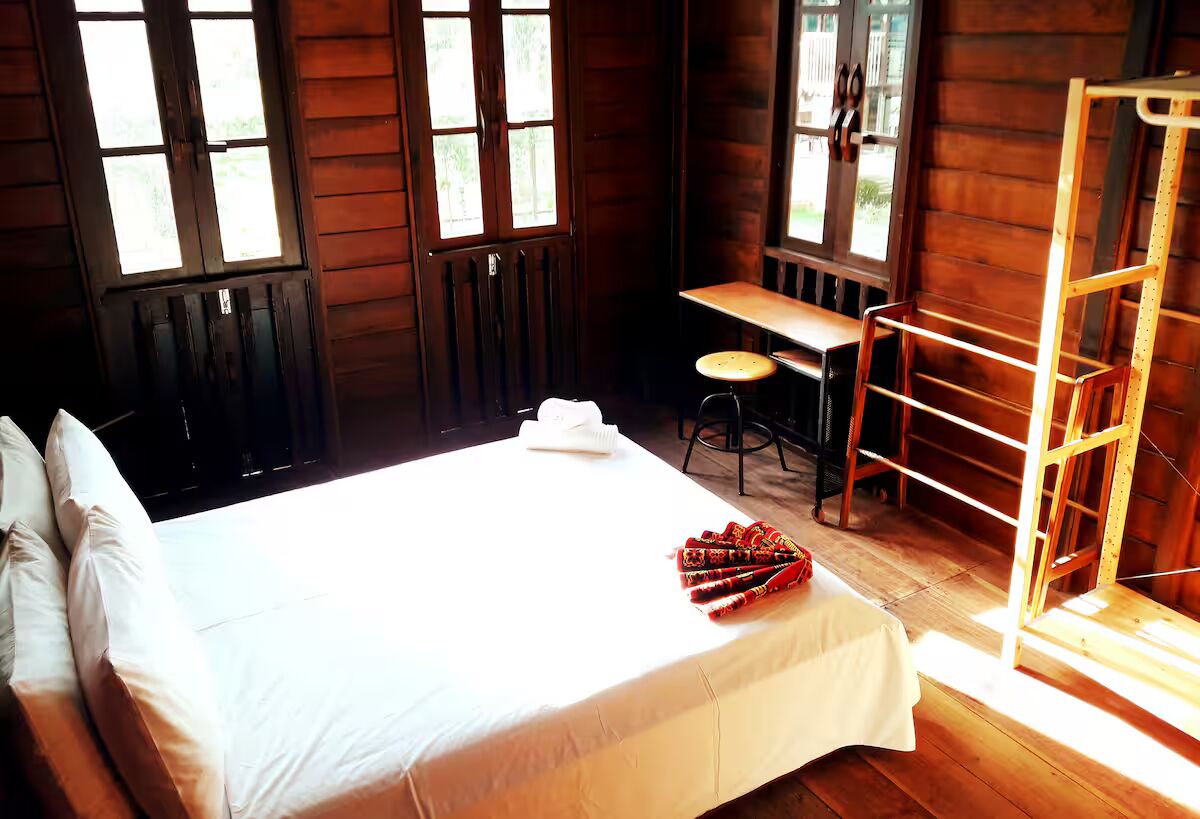 A wooden cabin room with a bed, a desk, and a chair.