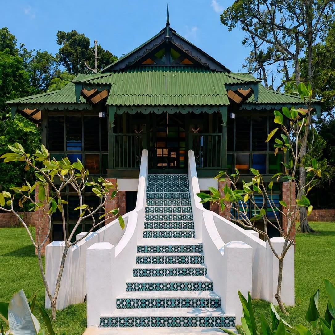 A building with a green roof, a staircase leading to the entrance, and a garden with trees and shrubs.
