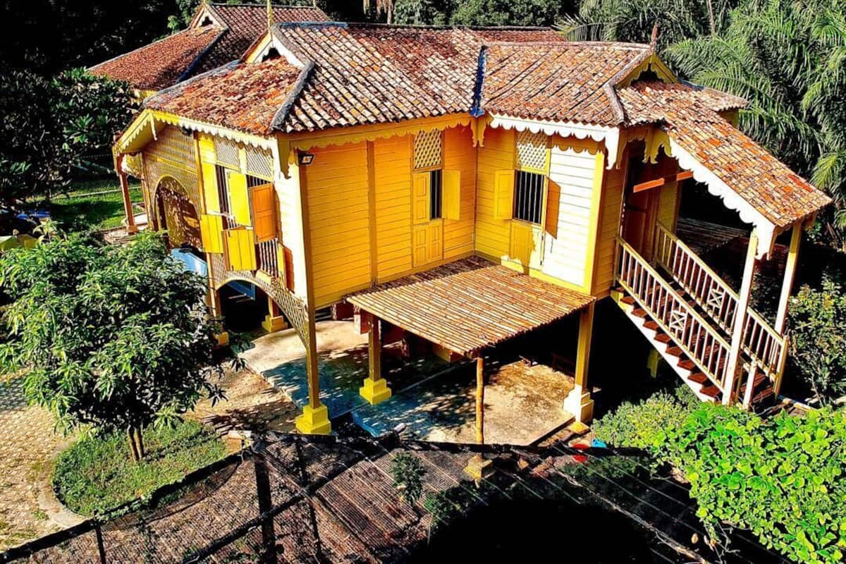 Une maison jaune avec un toit en tuiles, une véranda en bois et un escalier menant à un balcon.