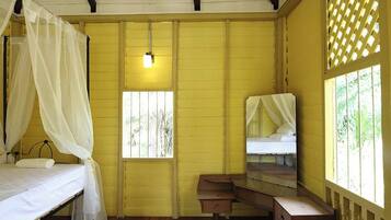 A room with two beds, one with a canopy, a small desk, and a window with bars.