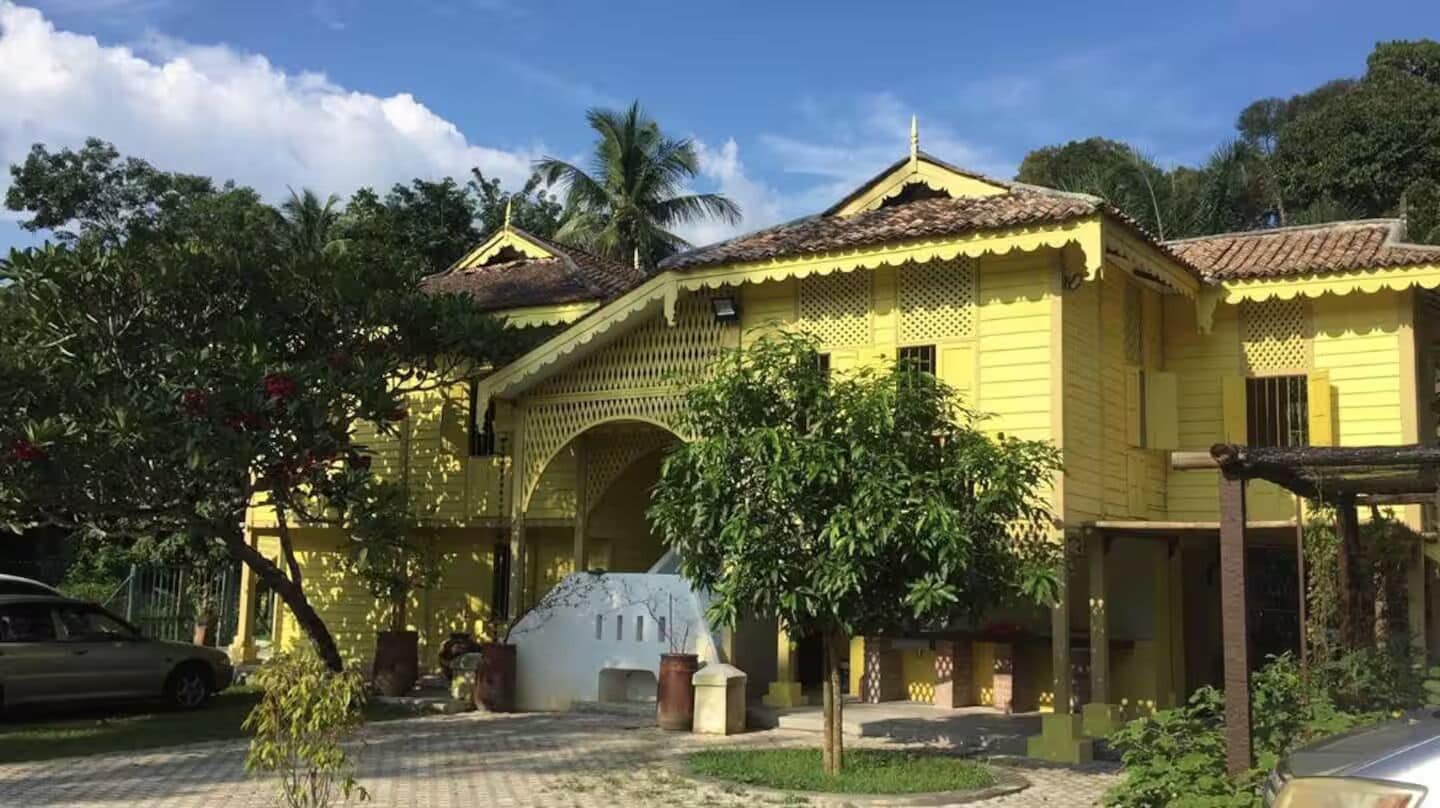 Un bâtiment jaune avec un toit en tuiles, une entrée couverte et une cour dallée.