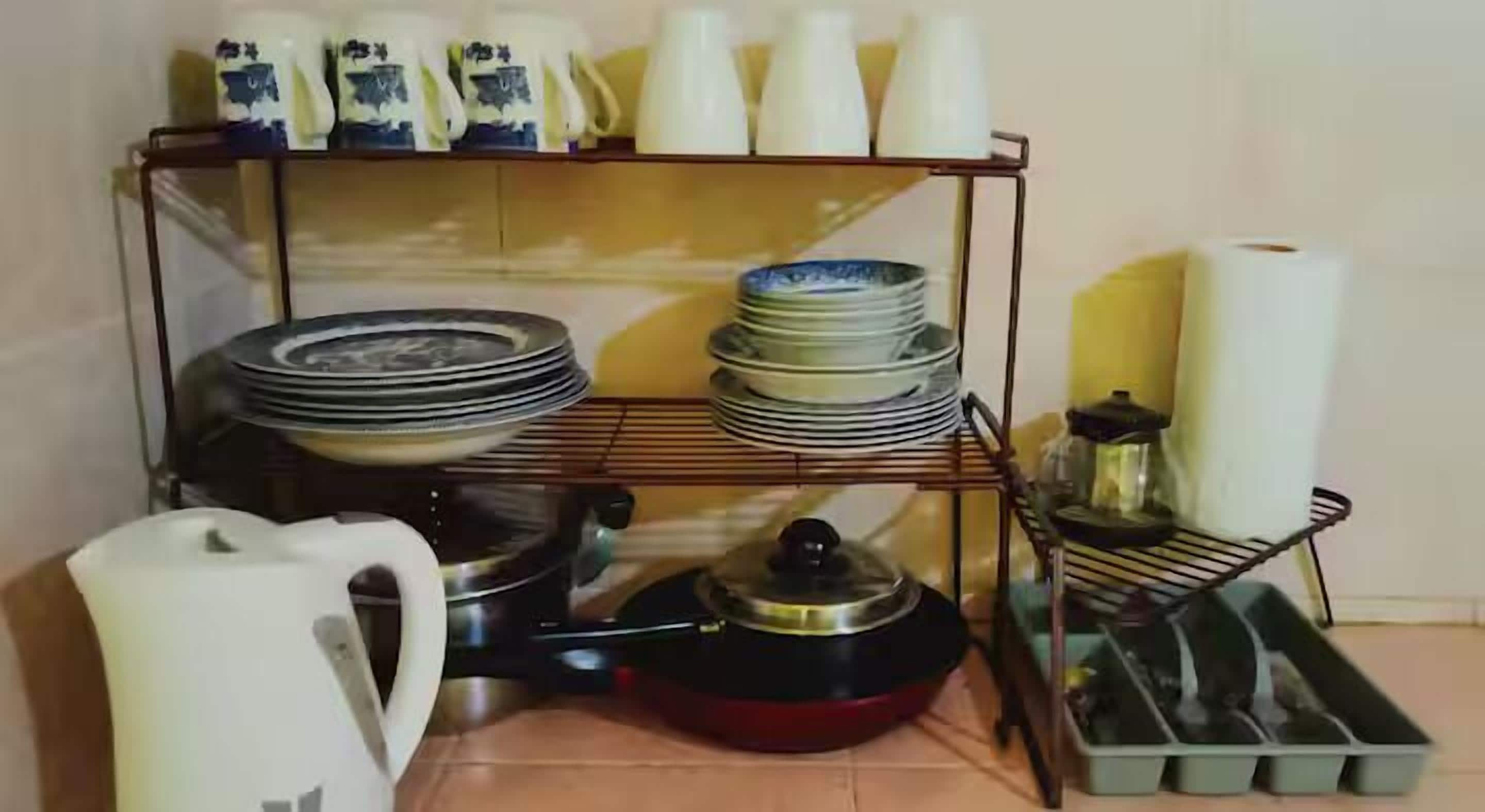 A kitchen area with a metal rack holding plates, bowls, and a kettle.