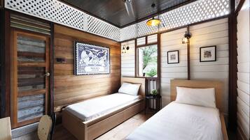 A wooden cabin-style room with two single beds, a wooden door, and a small table with a plant.