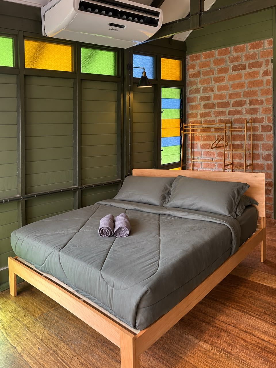 Una cama con colchón y almohadas grises, un marco de madera y un ventanal con vidrios de colores.