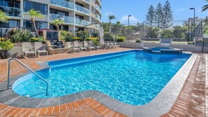 Une piscine avec des chaises longues et, au fond, un bâtiment doté de balcons.