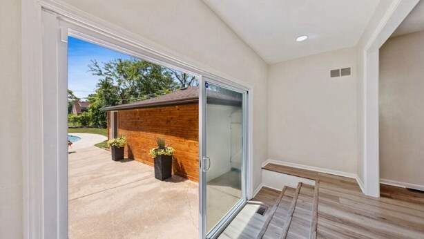 Un interior moderno con una puerta de cristal corredera que da a un patio, una terraza de madera y una pequeña construcción de ladrillo.