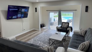Una sala moderna con una televisión de pantalla plana montada en la pared, un sofá, una mesa de centro y vistas a una piscina a través de una puerta de vidrio.