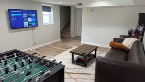 Una sala de estar con una mesa de futbolín, un televisor montado en la pared, un sofá y una mesa de centro.