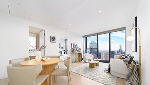A modern living room with a dining area, large windows with a city view, and minimalist decor.