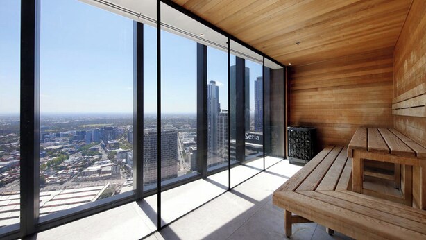 A high-rise room with large windows offering a city view, a wooden bench, and a tiled floor.