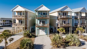 Un hotel frente a la playa con varios balcones, una entrada principal y palmeras.