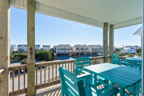 Une terrasse en bois, agrémentée de chaises et de tables turquoise, qui offre une vue sur une rangée de maisons.