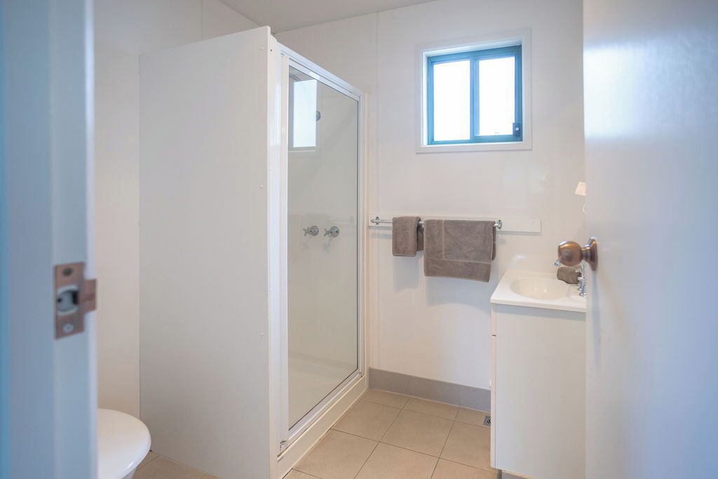 A bathroom with a glass-enclosed shower, a white sink, and a small window above the sink.
