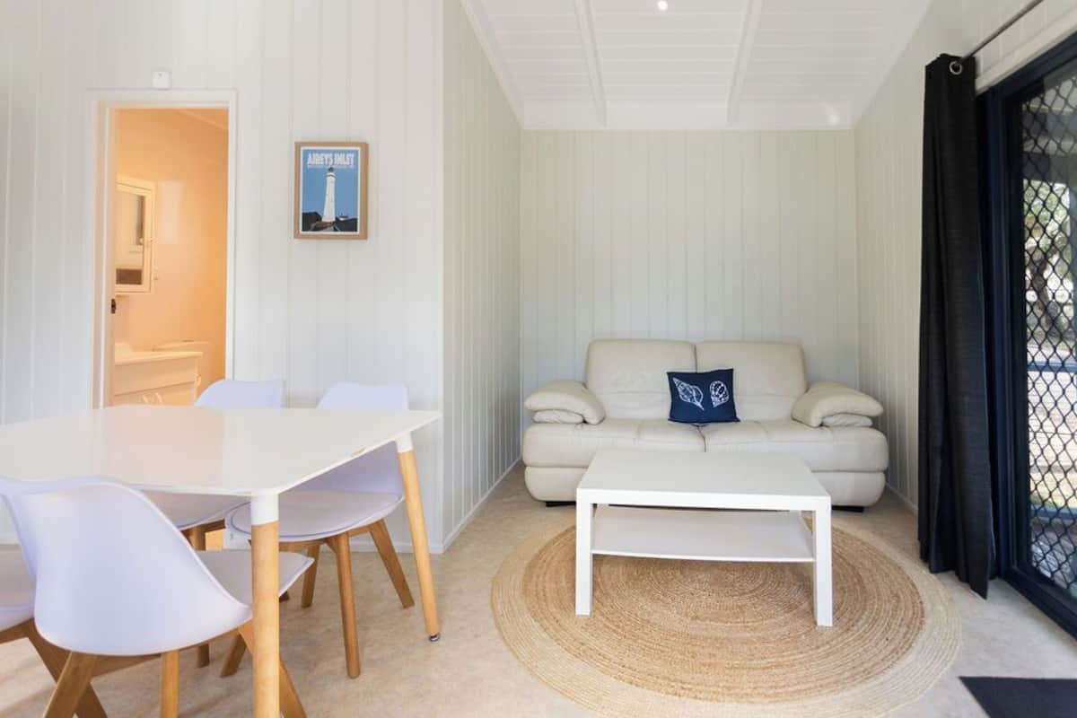 Ein modernes Wohnzimmer mit einem weißen Tisch und Stühlen, einem beige gefärbten Sofa mit blauem Kissen und einem weißen Couchtisch.