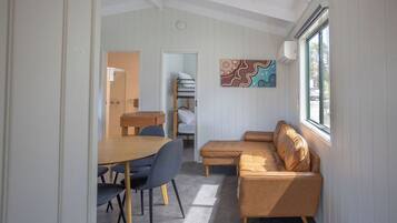 A cozy room with a wooden dining table, two blue chairs, a brown leather sofa, and a colorful wall art piece.