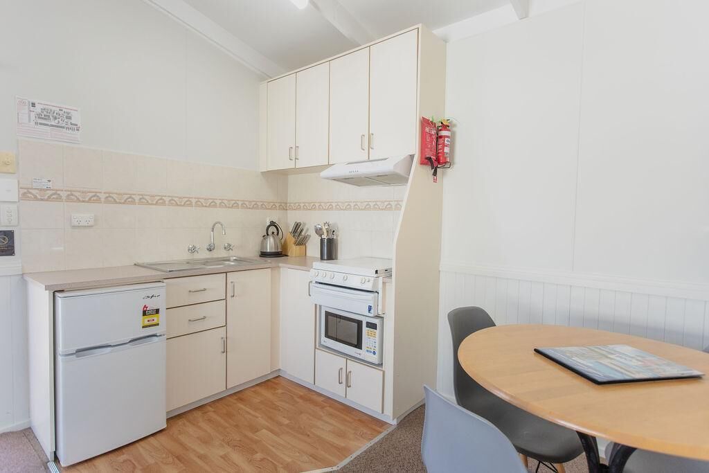 A compact kitchen with a refrigerator, oven, microwave, and sink. There is a small dining table with chairs.