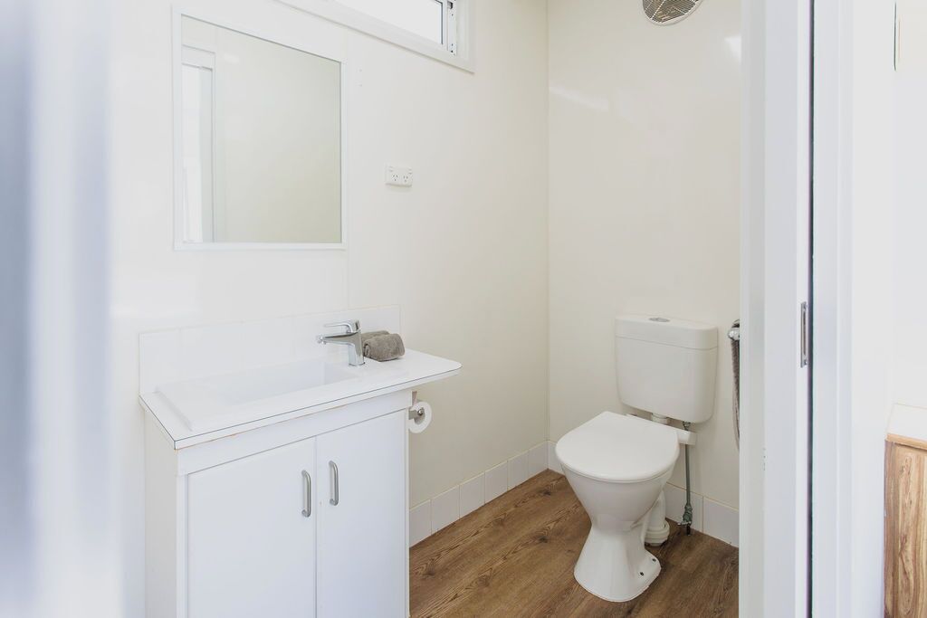 A small, clean bathroom with a white sink, mirror, and toilet.