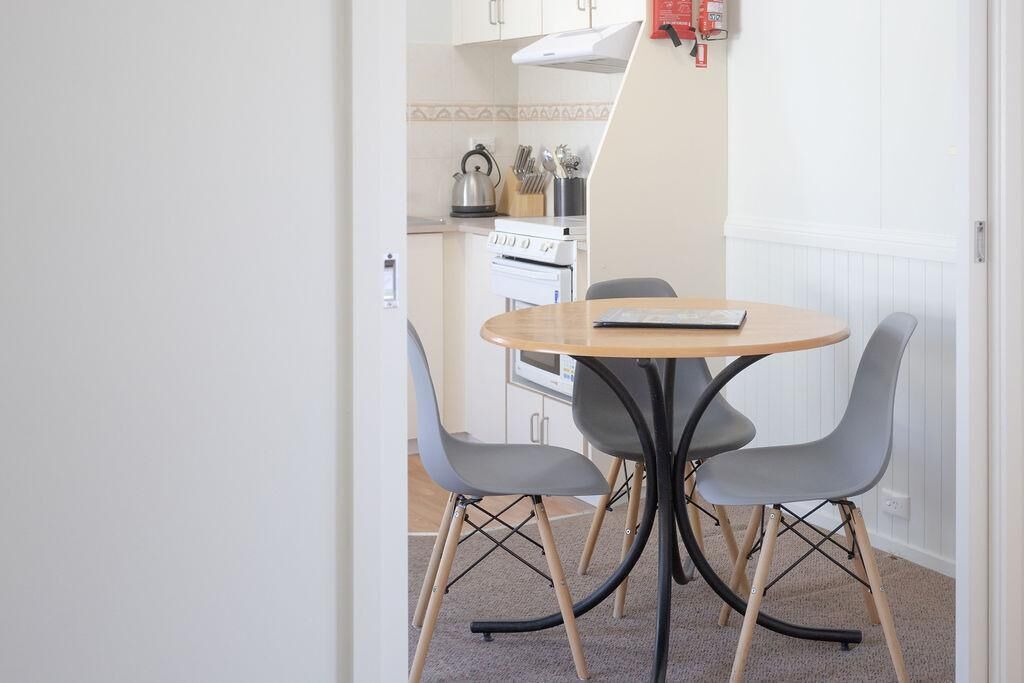 A small dining area with a round table and four chairs, a stove, and a kettle in the background.
