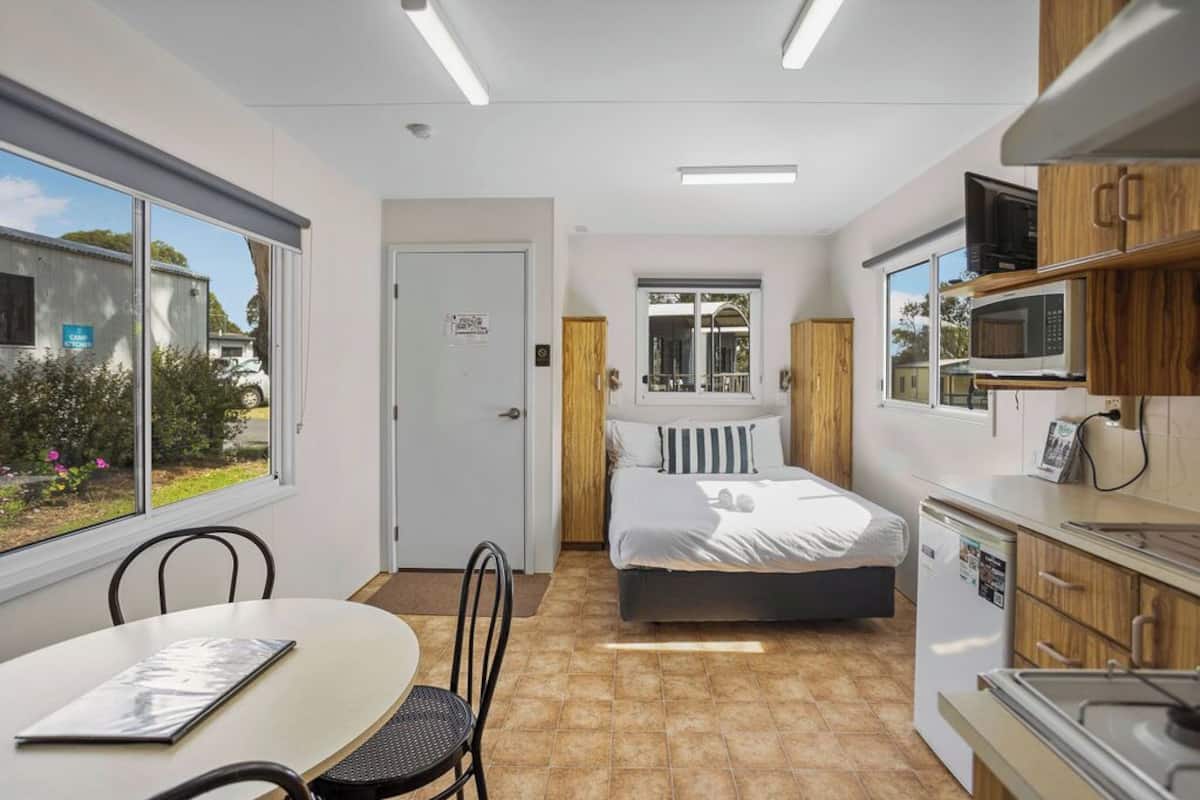 Ein kleines Zimmer mit Bett, einer Küchenzeile, einem Essbereich und einem Fenster mit Blick auf Grünflächen.