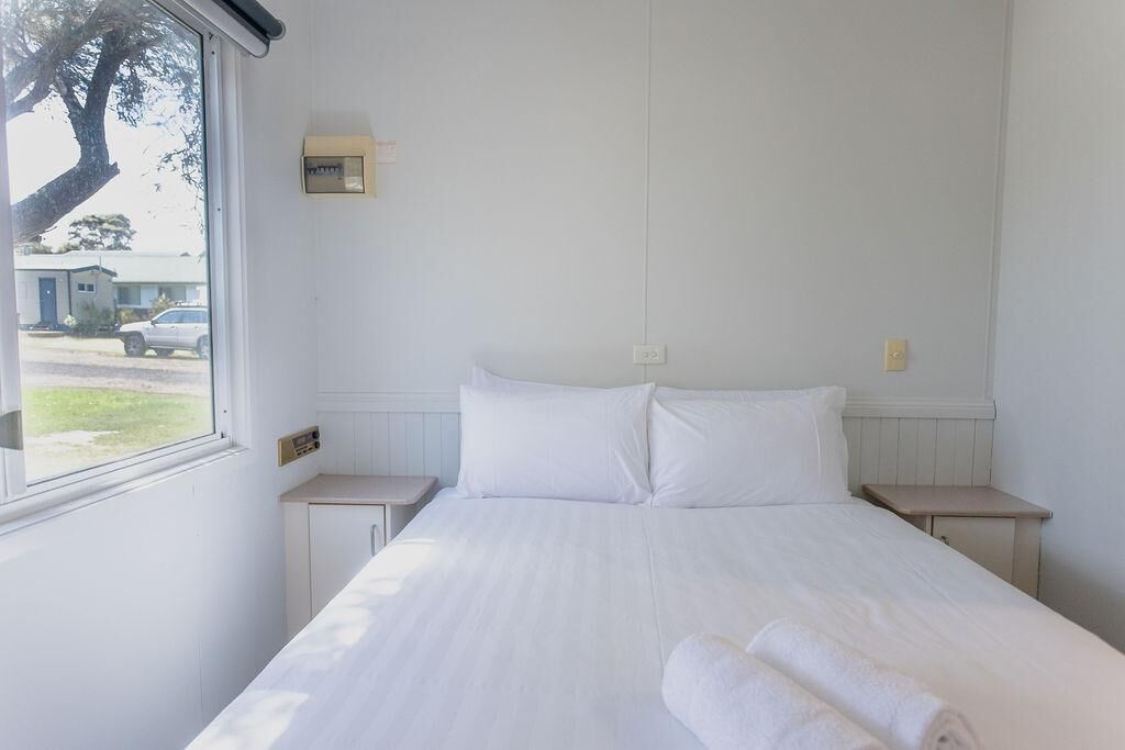 Une chambre avec un grand lit, deux tables de chevet, une fenêtre et un thermostat fixé au mur.