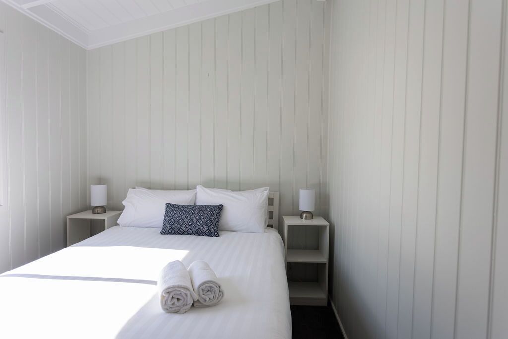 Un lit bien fait, avec du linge de lit blanc et deux oreillers, deux tables de chevet avec des lampes et une petite étagère.