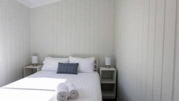 Un lit bien fait, avec du linge de lit blanc et deux oreillers, deux tables de chevet avec des lampes et une petite étagère.