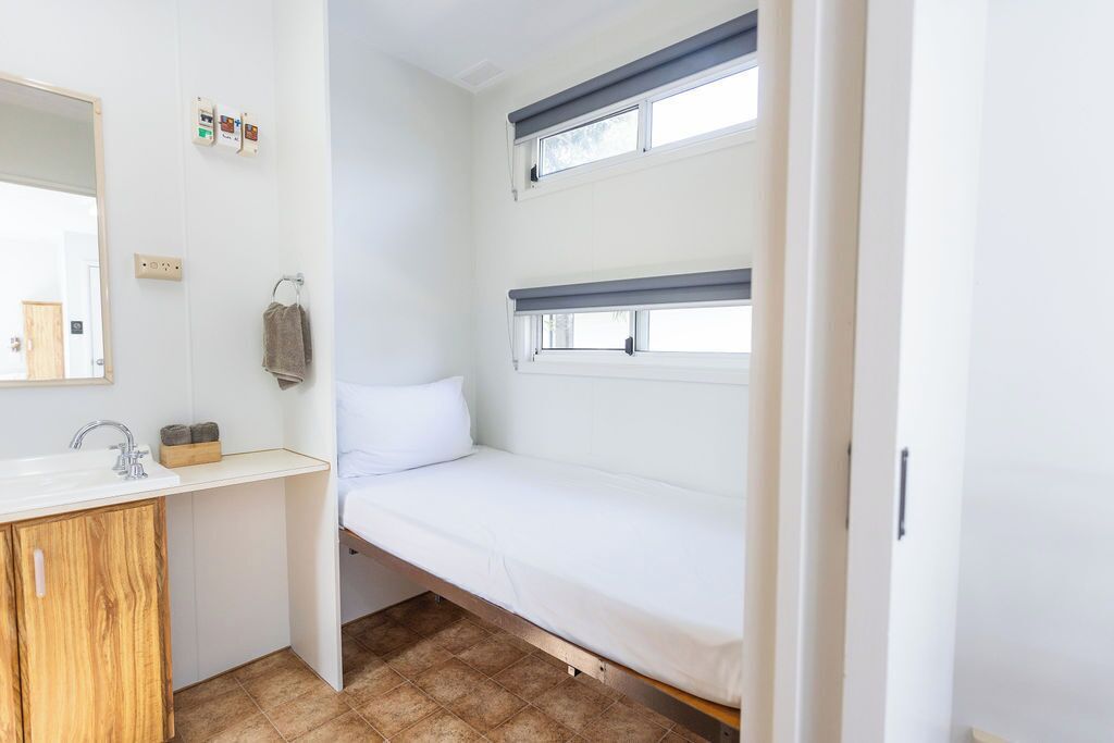 A compact room with a bunk bed, a small sink, and a mirror.