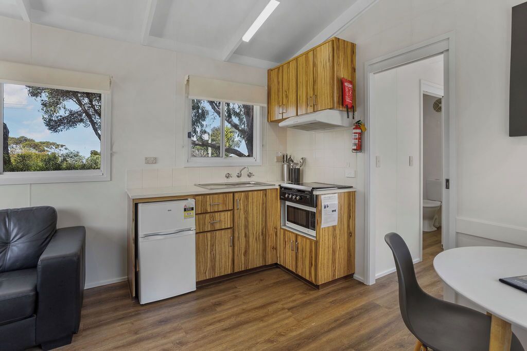 Une cuisine de taille réduite, dotée de meubles en bois, d’un réfrigérateur, d’une cuisinière et d’un évier. Un coin repas est aménagé avec une table et des chaises.