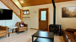 A living room with a wooden staircase, a fireplace, a television, and a sofa. - Lovekin Cabin - Prescott Cabin Rentals (Prescott)