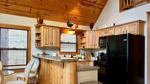 A kitchen with wooden cabinets, a black refrigerator, and a wooden island with chairs. - Lovekin Cabin - Prescott Cabin Rentals (Prescott)
