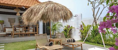 Un patio con mobiliario de mimbre, una sombrilla de paja y plantas en macetas.