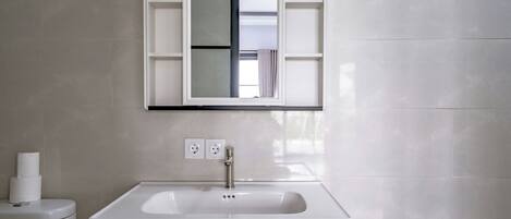 A bathroom with a white sink, a mirror above it, and a toilet to the left.