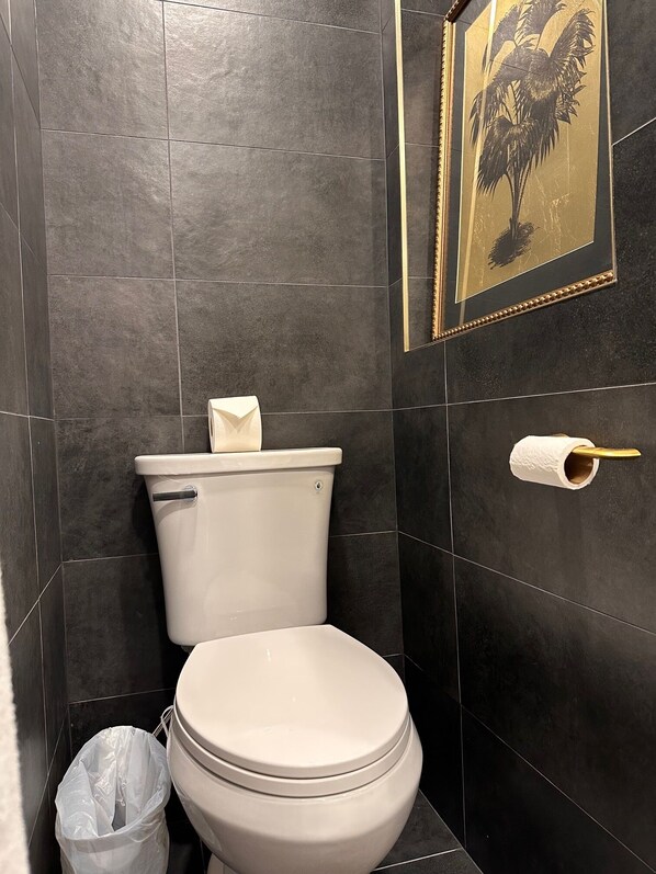 A bathroom with a toilet, a trash bin, and a toilet paper holder.