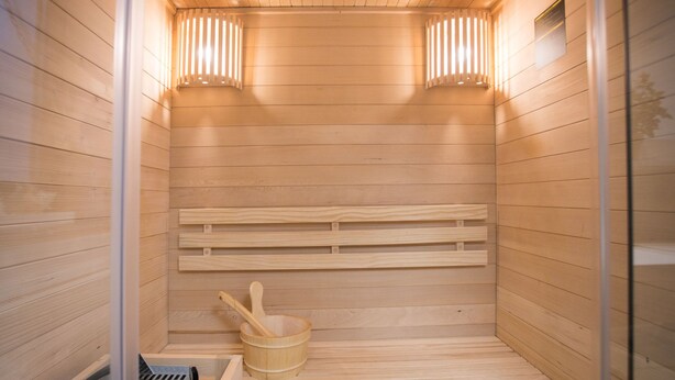 A sauna with wooden benches, a wooden bucket, and a stone-filled container. - Waldblick by Interhome (Winterberg)