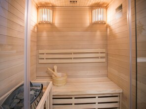Eine Sauna mit Holzbänken, einem Holzeimer und einem mit Steinen gefüllten Behälter.