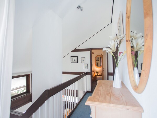 Eine Treppe mit hölzernem Geländer und weißen Spindeln, die zu einem Zwischenpodest mit Spiegel und gerahmten Bildern an der Wand führt.
