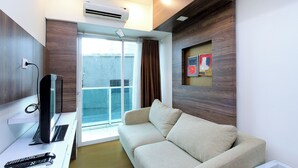 A modern living room with a sofa, a flat-screen TV, and a remote control on a white table. - La Grande by Djitu Hospitality (Bandung)