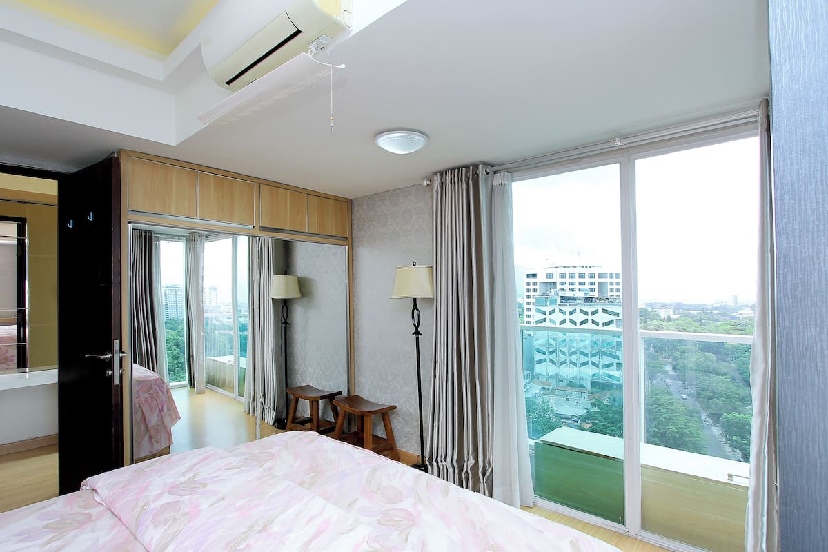 A hotel room with a large bed, a wardrobe, a desk, and a view of the city.