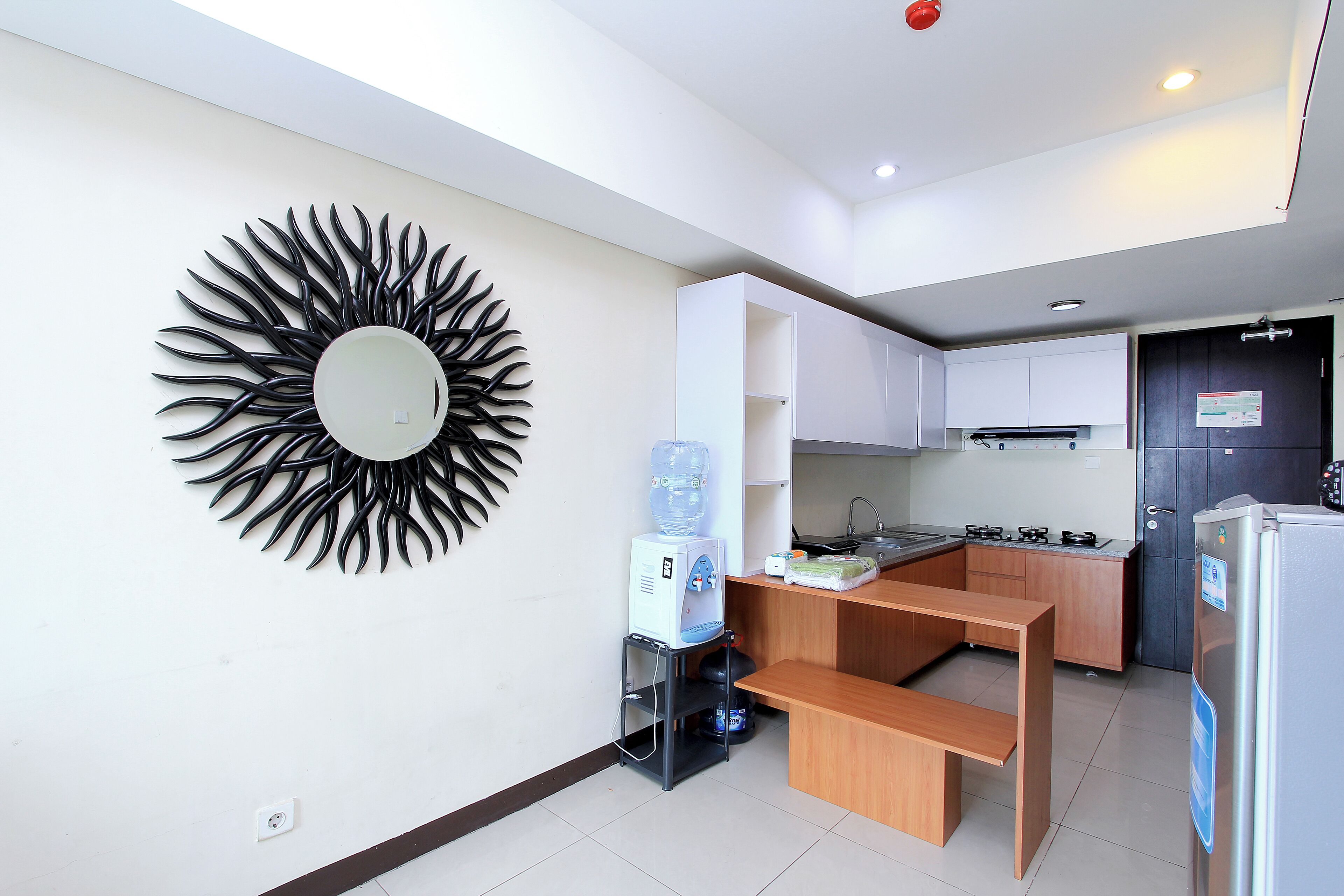 A modern kitchen with white cabinets, a water dispenser, a refrigerator, and a unique black sun-shaped wall decoration.