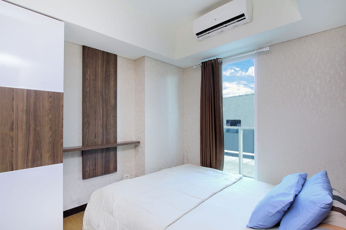 A hotel room with a bed, a window with curtains, a wall-mounted air conditioner, and a balcony with a view.
