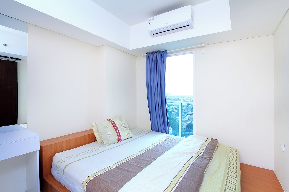 A bedroom with a bed, a desk, and a window with curtains.