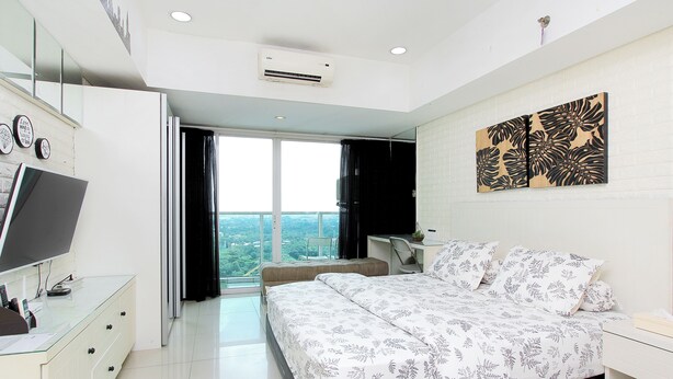 A modern bedroom with a large bed, a desk with a computer, a TV, and a balcony with a city view. - La Grande by Djitu Hospitality (Bandung)